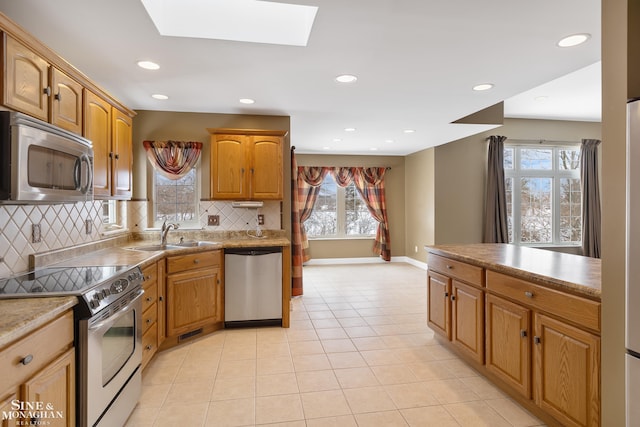 kitchen with stainless steel appliances, sink, light tile patterned floors, a skylight, and decorative backsplash