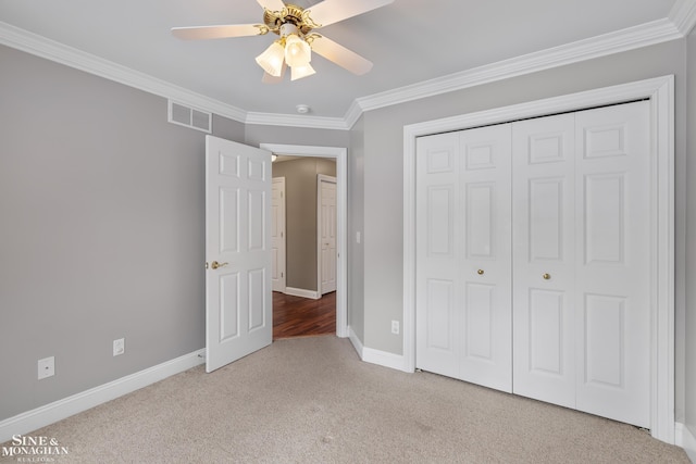 unfurnished bedroom featuring ceiling fan, a closet, crown molding, and light colored carpet