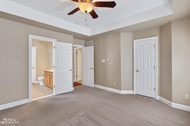 unfurnished bedroom featuring ceiling fan, a raised ceiling, light carpet, and ensuite bathroom