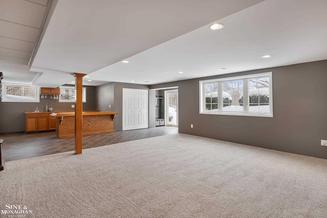 unfurnished living room featuring dark colored carpet, a wealth of natural light, and indoor bar