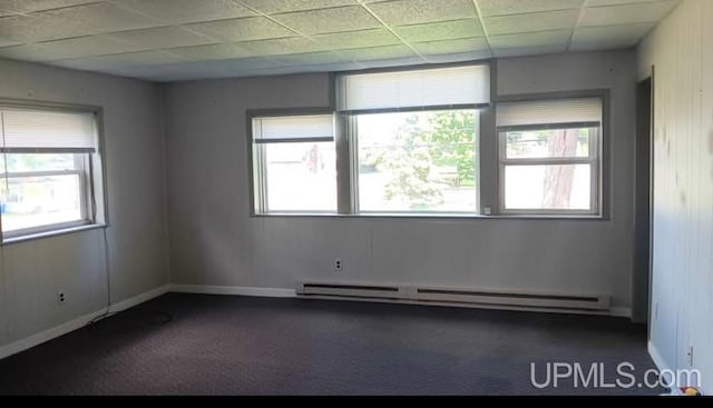 empty room featuring dark colored carpet, a paneled ceiling, and a baseboard heating unit