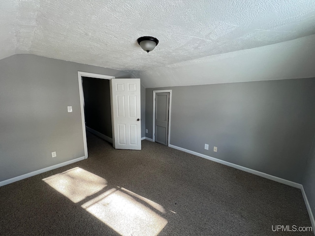 unfurnished bedroom with a textured ceiling, a closet, lofted ceiling, and carpet flooring