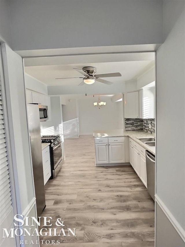 kitchen with white cabinets, stainless steel appliances, light countertops, light wood-style floors, and backsplash