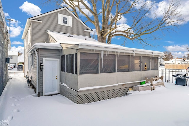 snow covered rear of property featuring a sunroom