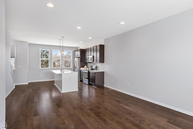 kitchen with appliances with stainless steel finishes, dark brown cabinets, an island with sink, dark hardwood / wood-style flooring, and sink