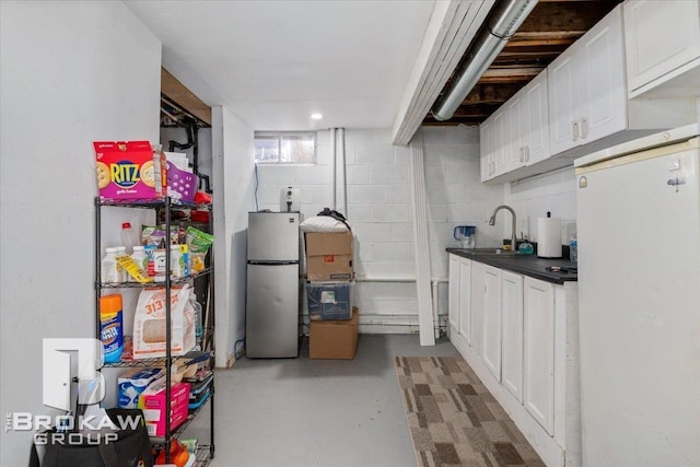 interior space featuring freestanding refrigerator, a sink, and concrete block wall