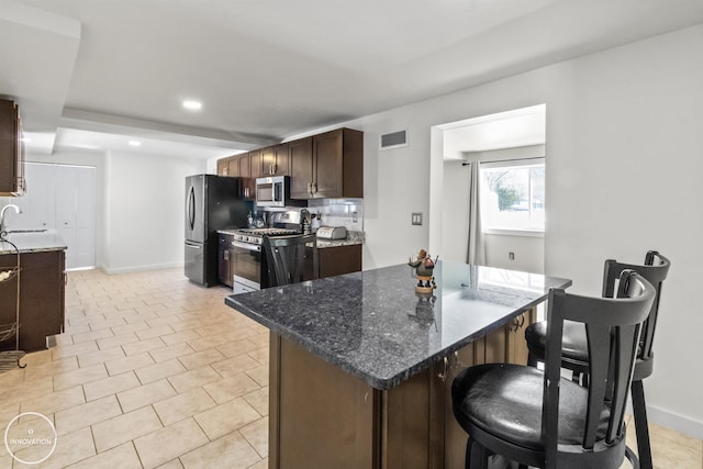 kitchen featuring dark stone countertops, light tile patterned floors, sink, stainless steel appliances, and a breakfast bar area