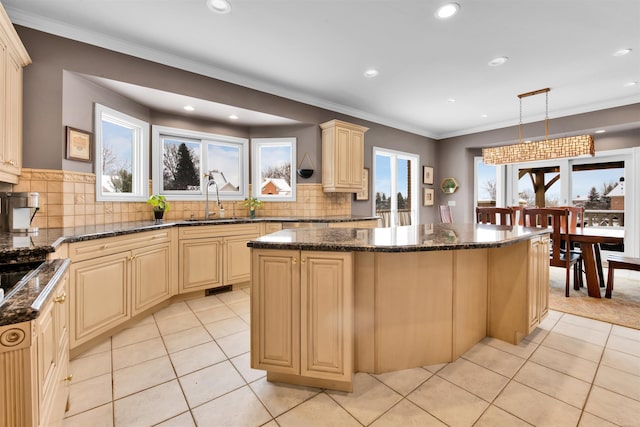 kitchen with dark stone countertops, sink, pendant lighting, a kitchen island, and ornamental molding