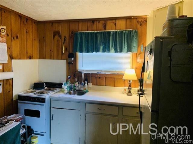 kitchen with white electric range, a textured ceiling, wood walls, sink, and black fridge