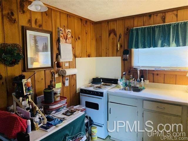 kitchen with wood walls, sink, white electric range oven, and a textured ceiling