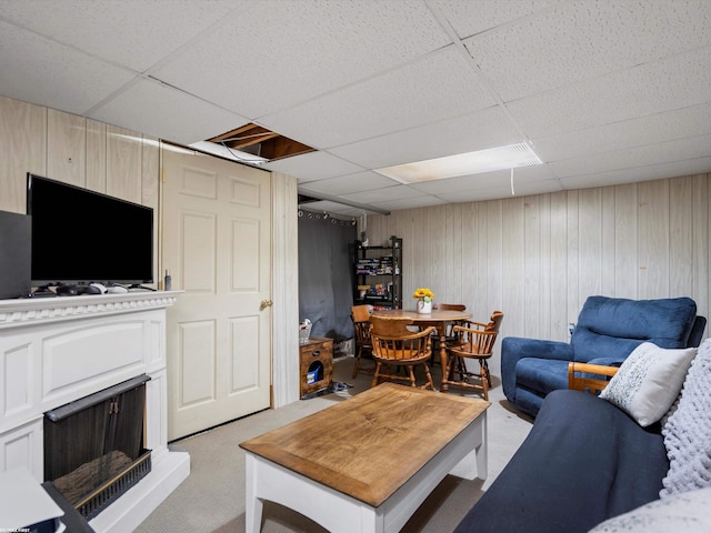 living room featuring a fireplace with raised hearth, a drop ceiling, and light colored carpet