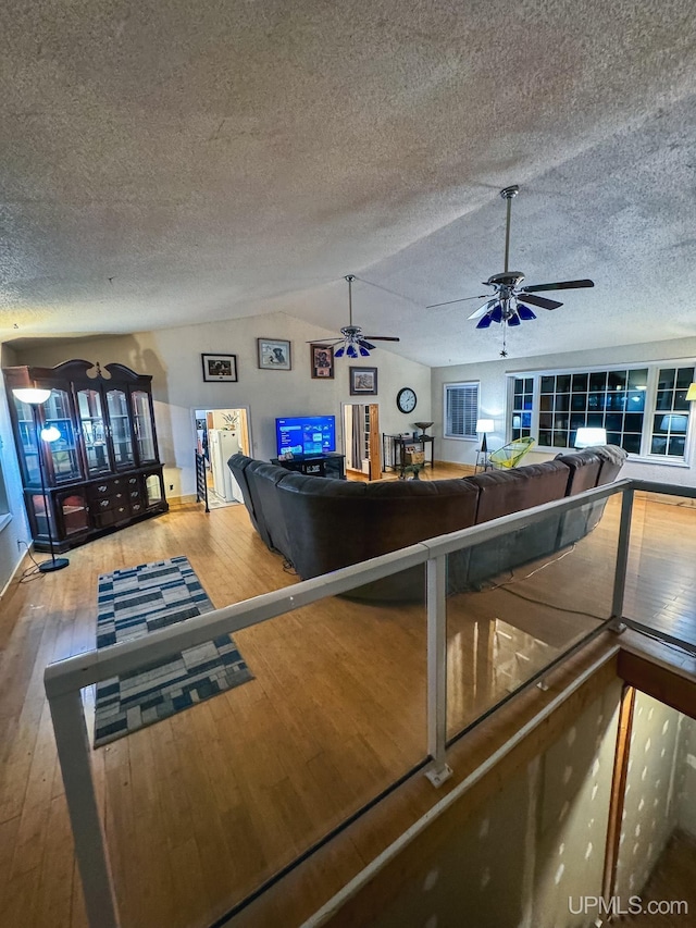 interior space featuring a textured ceiling, a ceiling fan, vaulted ceiling, and wood finished floors