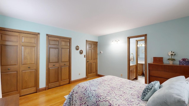 bedroom with baseboards, ensuite bath, light wood-style flooring, and multiple closets