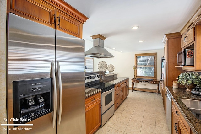 kitchen featuring appliances with stainless steel finishes, brown cabinetry, light tile patterned flooring, island range hood, and dark stone counters