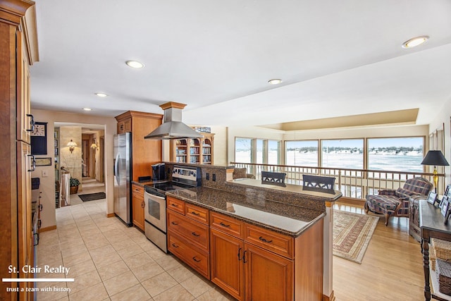 kitchen featuring island range hood, brown cabinets, dark stone countertops, open floor plan, and stainless steel appliances