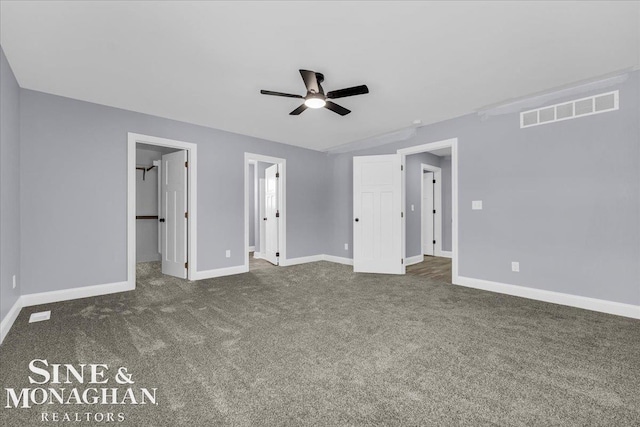 unfurnished bedroom featuring carpet floors, a walk in closet, visible vents, a ceiling fan, and baseboards