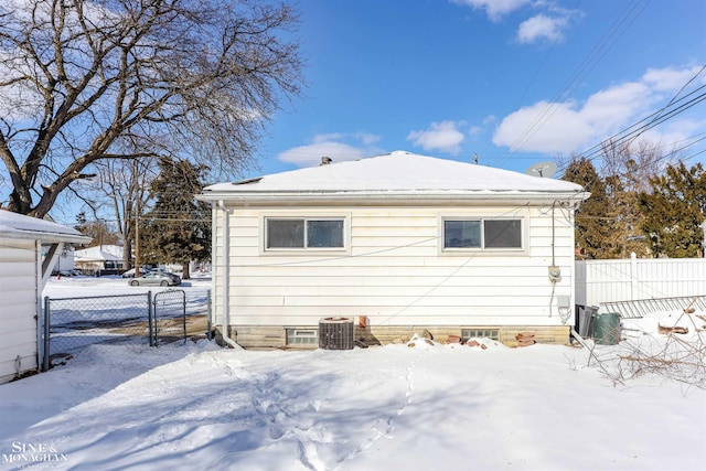 snow covered rear of property with cooling unit and fence