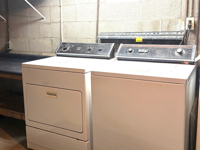 clothes washing area featuring concrete block wall and washing machine and clothes dryer