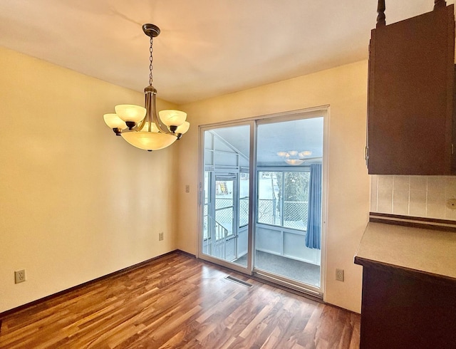 unfurnished dining area featuring baseboards, wood finished floors, visible vents, and a notable chandelier