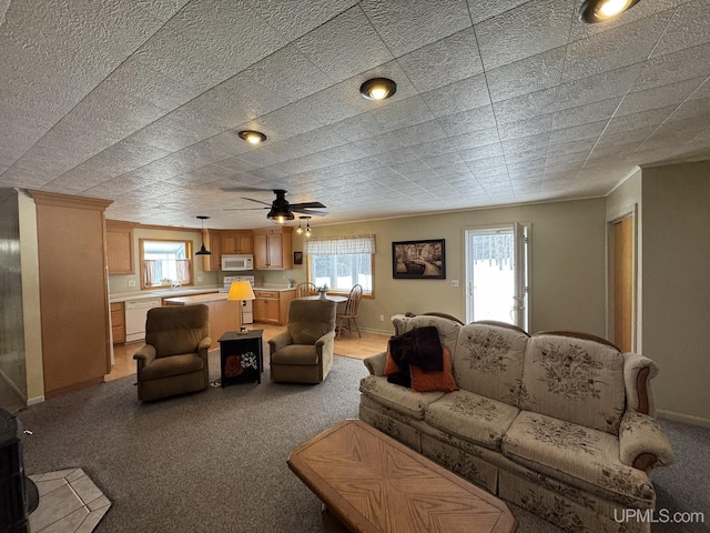 living area featuring light carpet, baseboards, a ceiling fan, and ornamental molding