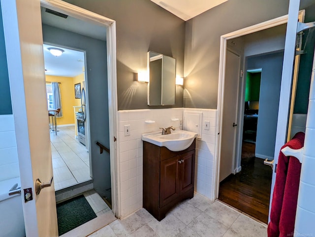 bathroom with visible vents, a wainscoted wall, tile patterned flooring, vanity, and tile walls