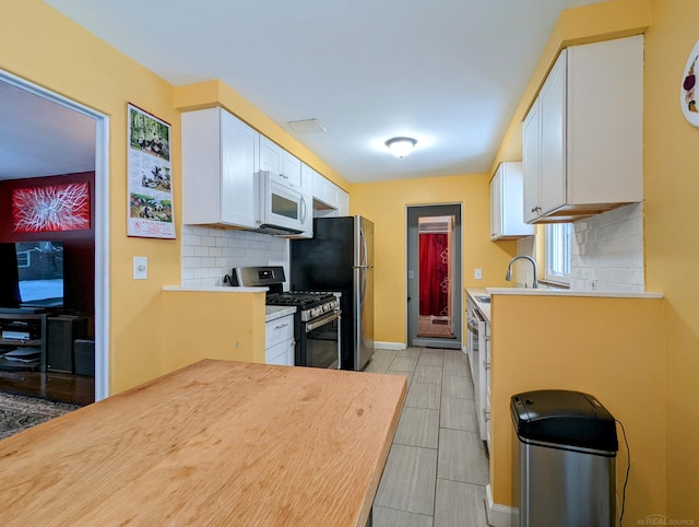 kitchen with appliances with stainless steel finishes, light countertops, white cabinetry, and tasteful backsplash