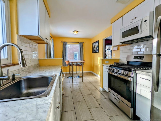 kitchen with white cabinets, baseboards, stainless steel appliances, and a sink