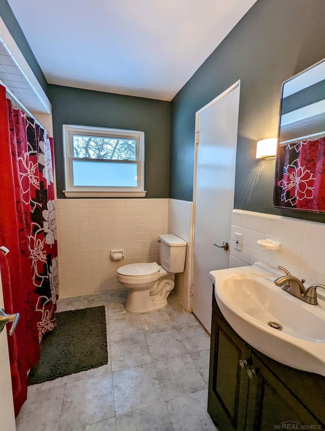 full bathroom featuring tile patterned flooring, toilet, a wainscoted wall, vanity, and tile walls