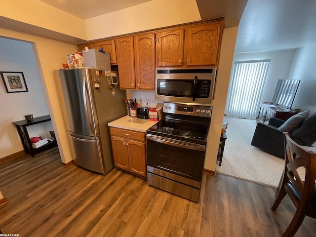 kitchen featuring brown cabinets, dark wood-type flooring, stainless steel appliances, and light countertops