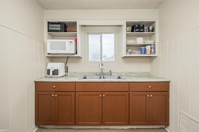 kitchen with visible vents, white microwave, light countertops, open shelves, and a sink