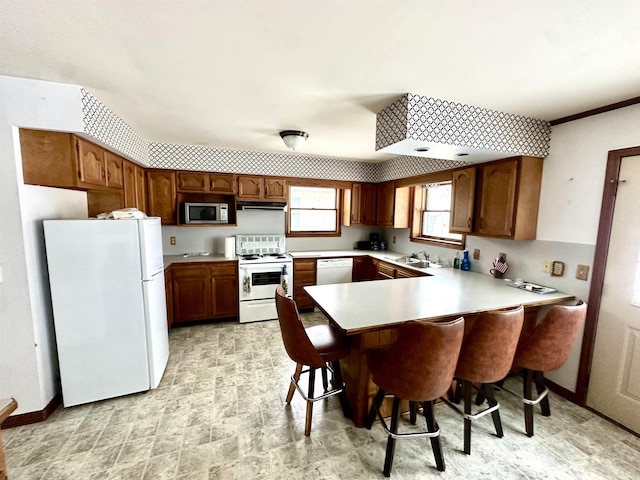 kitchen featuring a peninsula, white appliances, a sink, light countertops, and brown cabinetry