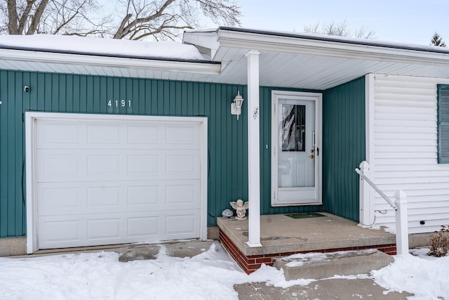 snow covered property entrance with a garage