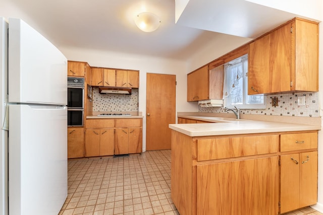 kitchen with light countertops, decorative backsplash, brown cabinetry, white appliances, and a peninsula