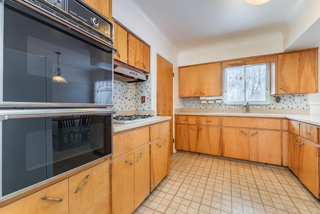 kitchen with under cabinet range hood, white gas cooktop, a sink, light countertops, and backsplash