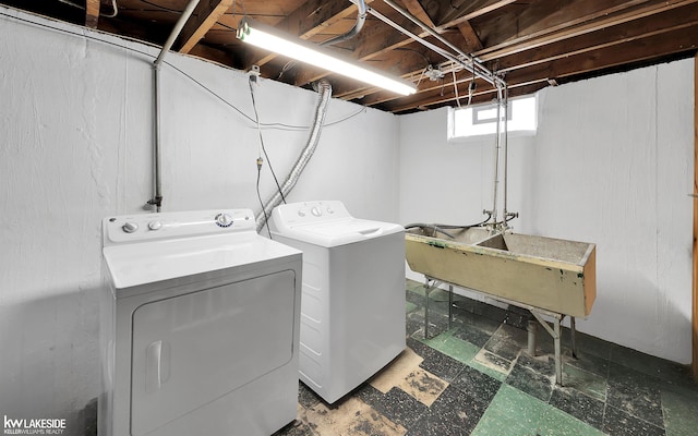 clothes washing area with laundry area, dark floors, washer and clothes dryer, and a sink