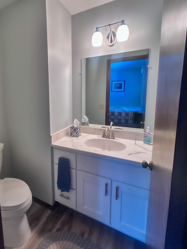 half bathroom with connected bathroom, vanity, toilet, and wood finished floors