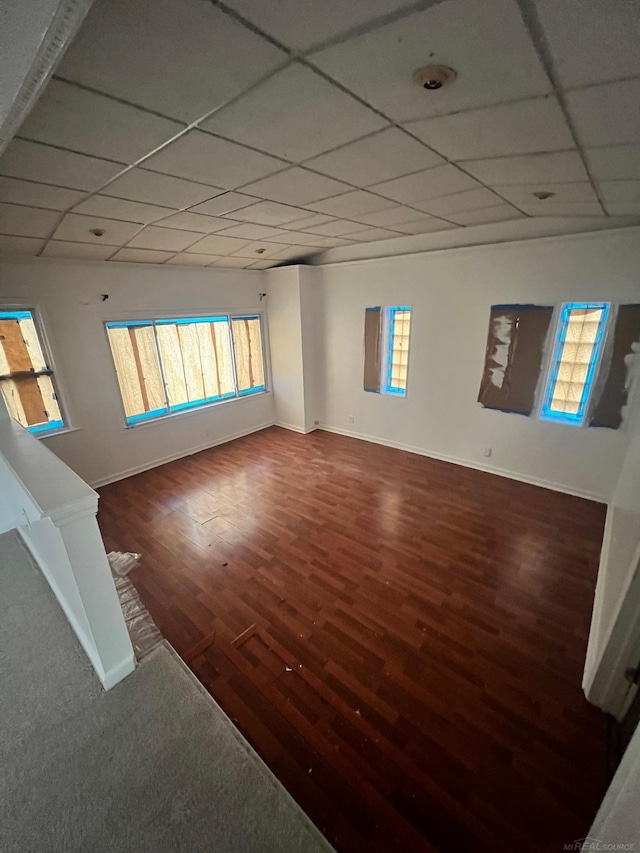 empty room featuring a paneled ceiling, baseboards, and dark wood-style flooring