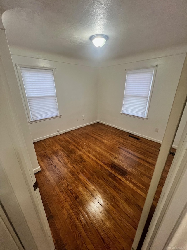 empty room with dark wood-style floors, a wealth of natural light, visible vents, and baseboards