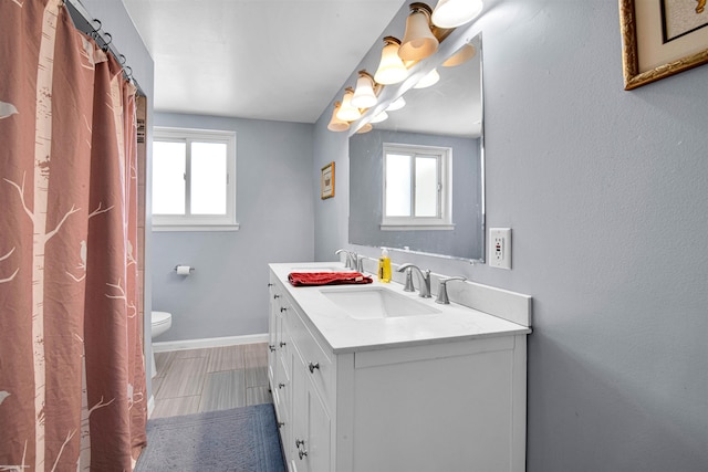 bathroom with baseboards, a sink, toilet, and double vanity