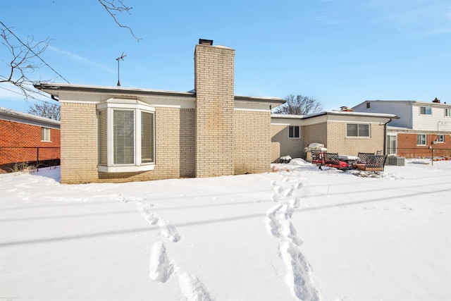 snow covered property with a chimney and brick siding