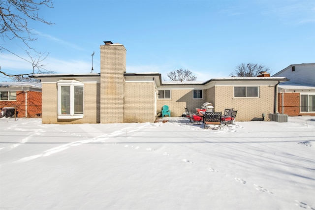 snow covered rear of property with brick siding and a chimney