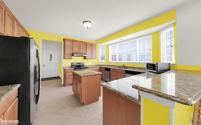 kitchen featuring light tile patterned floors, under cabinet range hood, a center island, appliances with stainless steel finishes, and light stone countertops