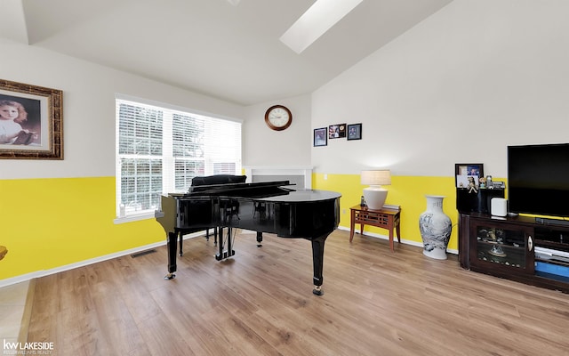 sitting room with light wood-type flooring, visible vents, vaulted ceiling with skylight, and baseboards