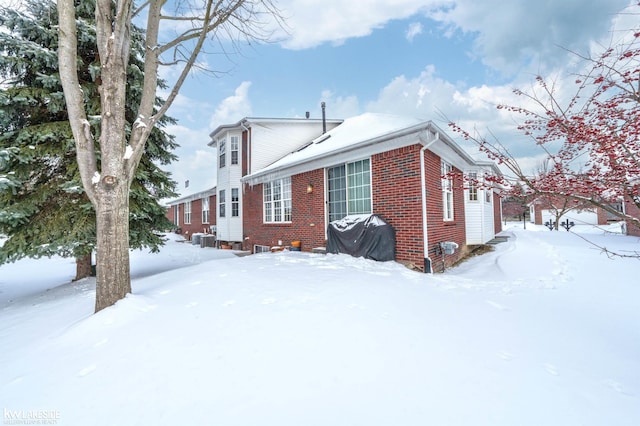 snow covered rear of property featuring brick siding