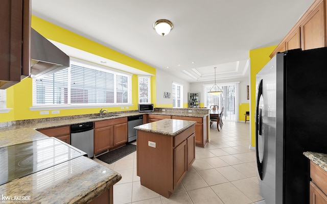 kitchen with a tray ceiling, a center island, brown cabinets, appliances with stainless steel finishes, and a peninsula