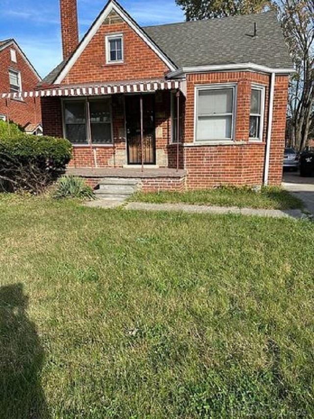 view of front of house featuring brick siding, roof with shingles, a chimney, covered porch, and a front lawn