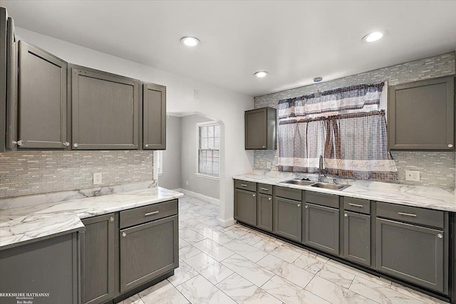 kitchen featuring arched walkways, baseboards, decorative backsplash, marble finish floor, and a sink