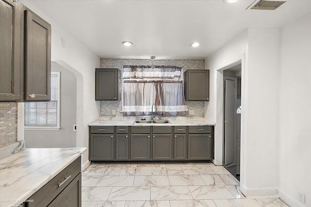 kitchen featuring marble finish floor, visible vents, decorative backsplash, a sink, and dark brown cabinetry