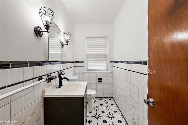 half bathroom with tile walls, wainscoting, vanity, and toilet