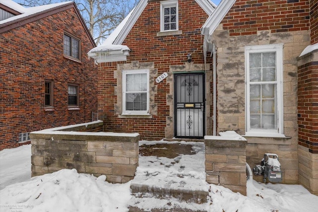 snow covered property entrance with stone siding and brick siding